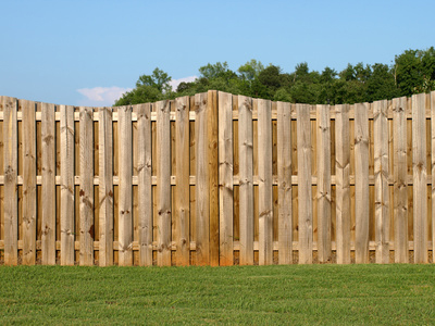 Wooden fence along a back yard with grass and blue sky